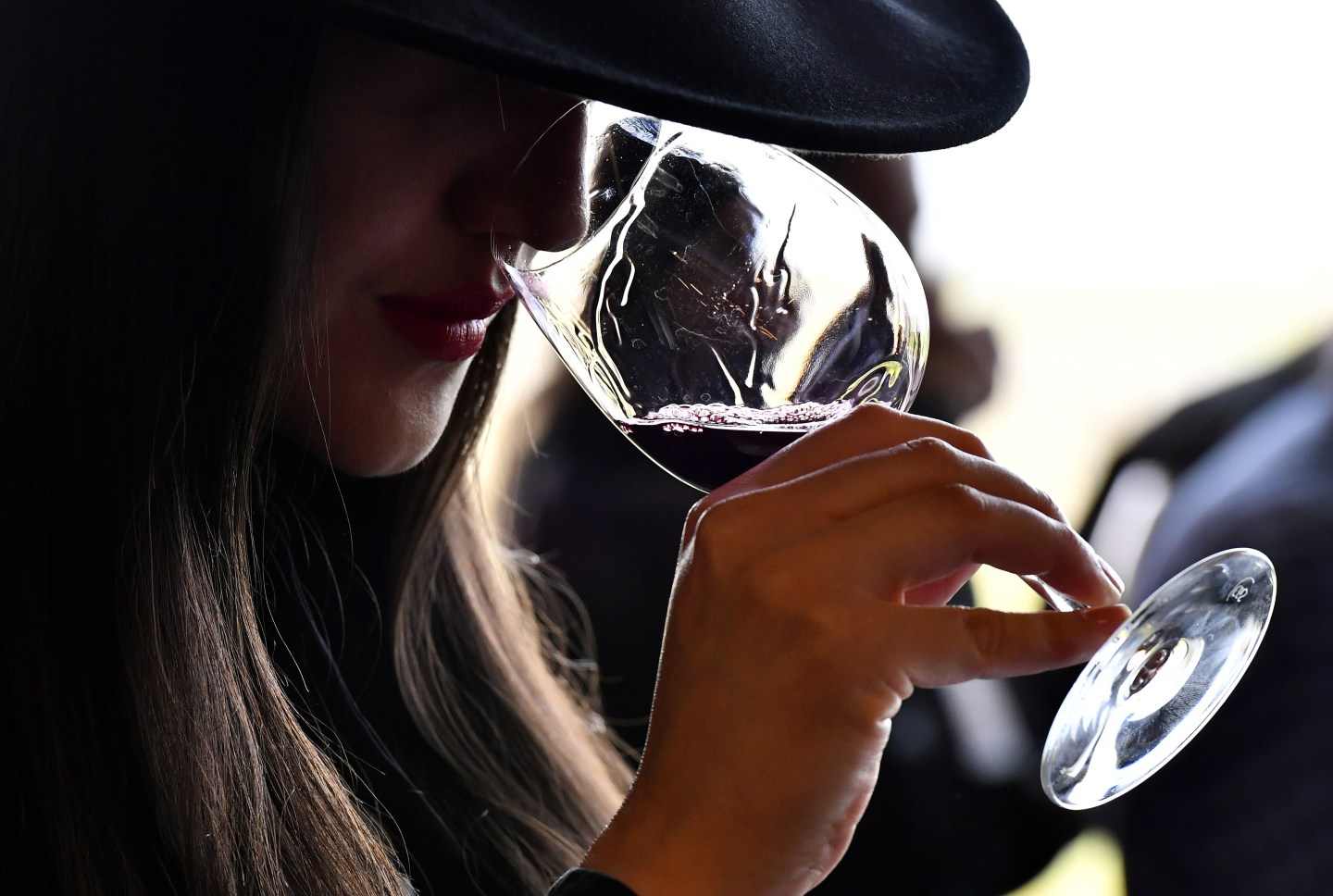 Woman in hat smells glass of red wine