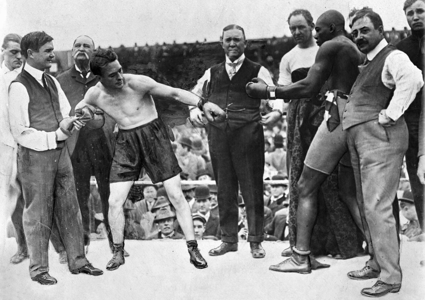 Stanley Ketchel and Jack Johnson touch gloves in the ring, surrounded by officials, before their fight