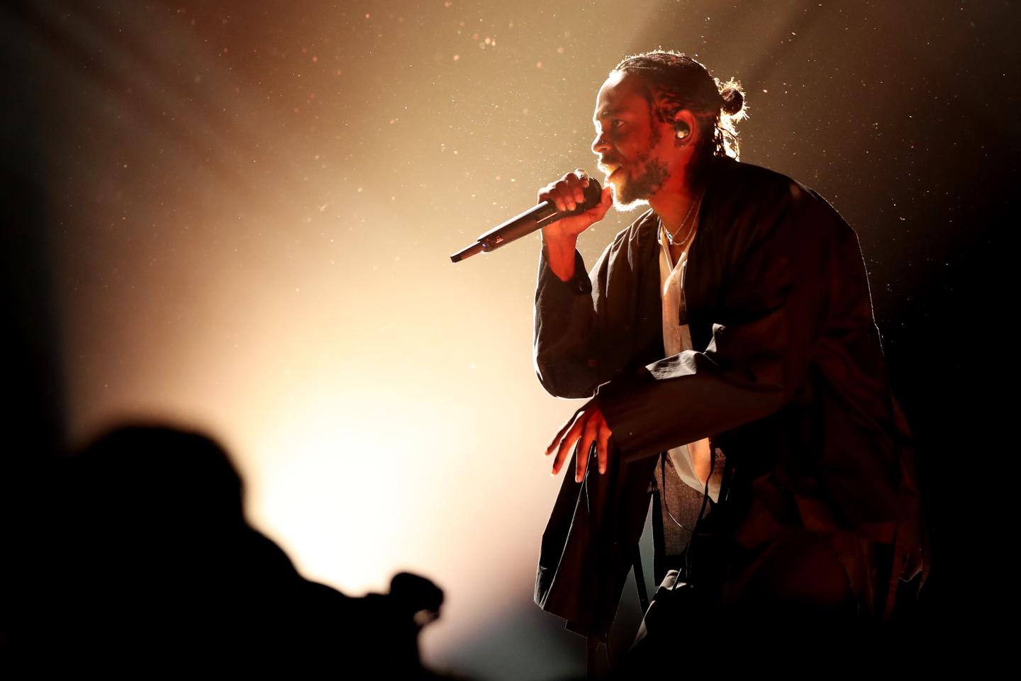 Kendrick Lamar, ringed in light, looks out over the crowd while holding a microphone during his Grammy performance.