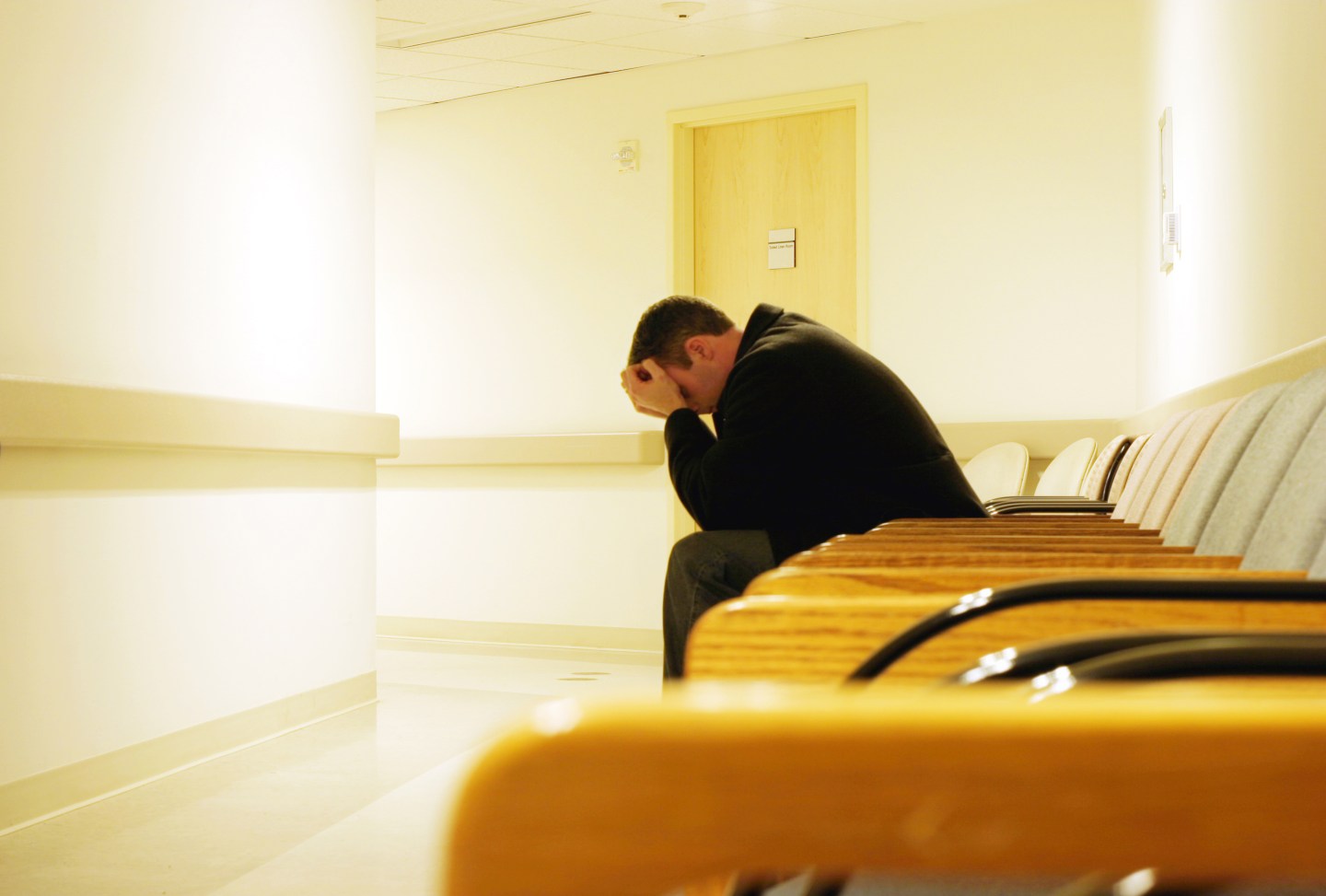 Man sits in doctor's office waiting room with his heads in his hands.