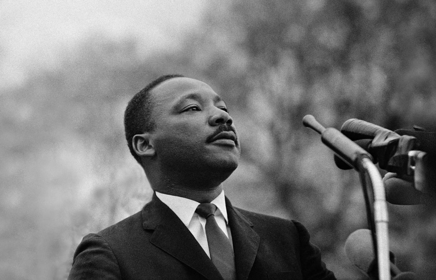 Dr. Martin Luther King, Jr. stands in front of several microphones and looks over a crowd of 25,000 out of frame in front of him