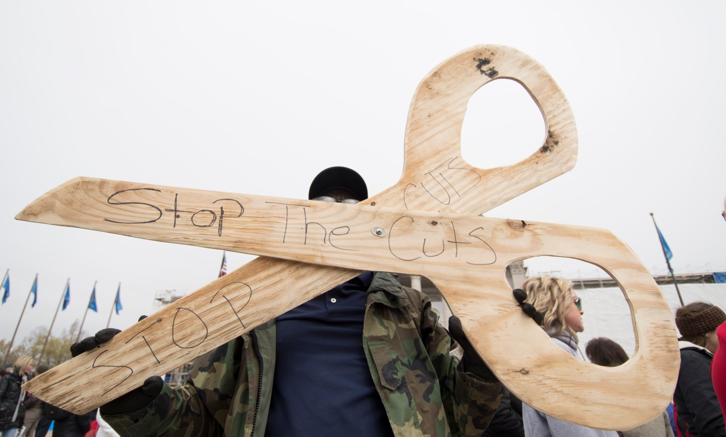 A man holds a giant pair of wooden scissors that read "stop the cuts" at a protest of teachers in Oklahoma