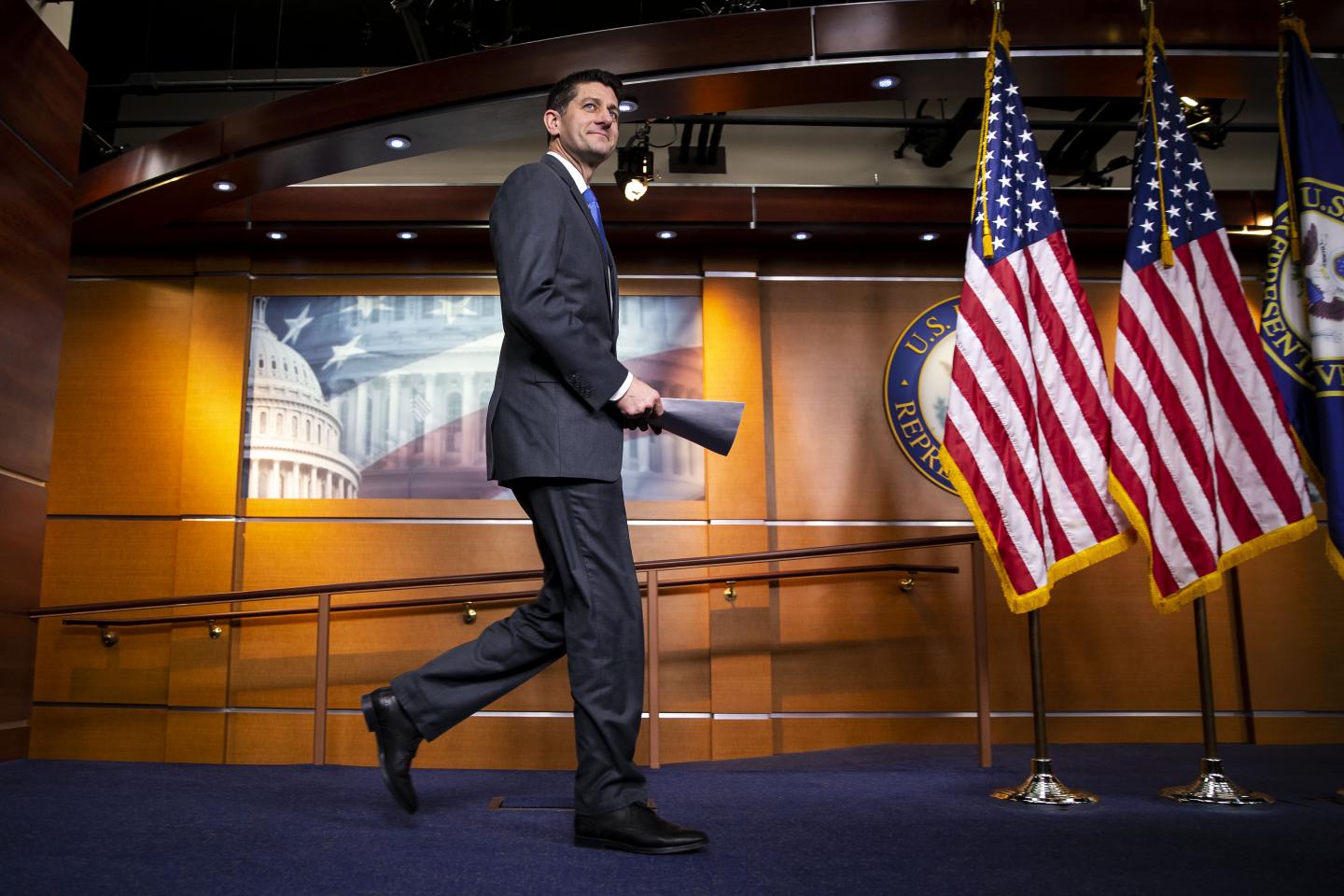 House Speaker Paul Ryan holds a stack of papers and walks off stage toward two American flags after announcing at a press conference that he won't seek re-election in November.