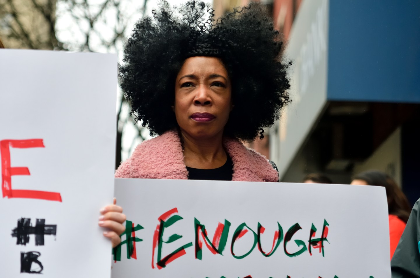 A woman with voluminous natural hair holds a sign that says "#Enough"