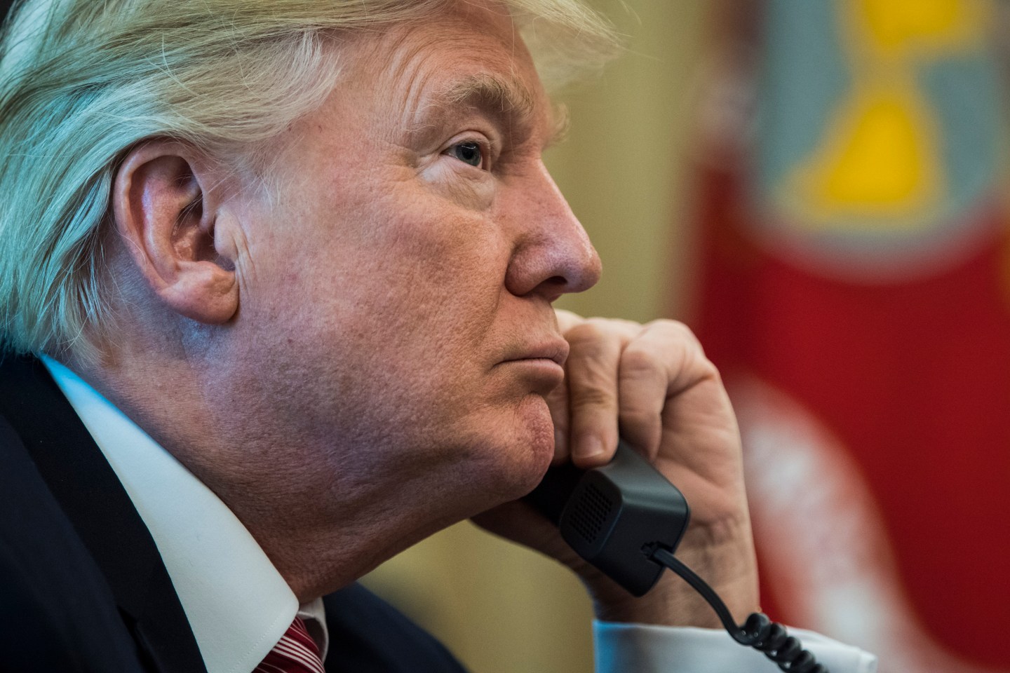 President Donald Trump holds a phone up to his left ear with the right side of his face in profile.