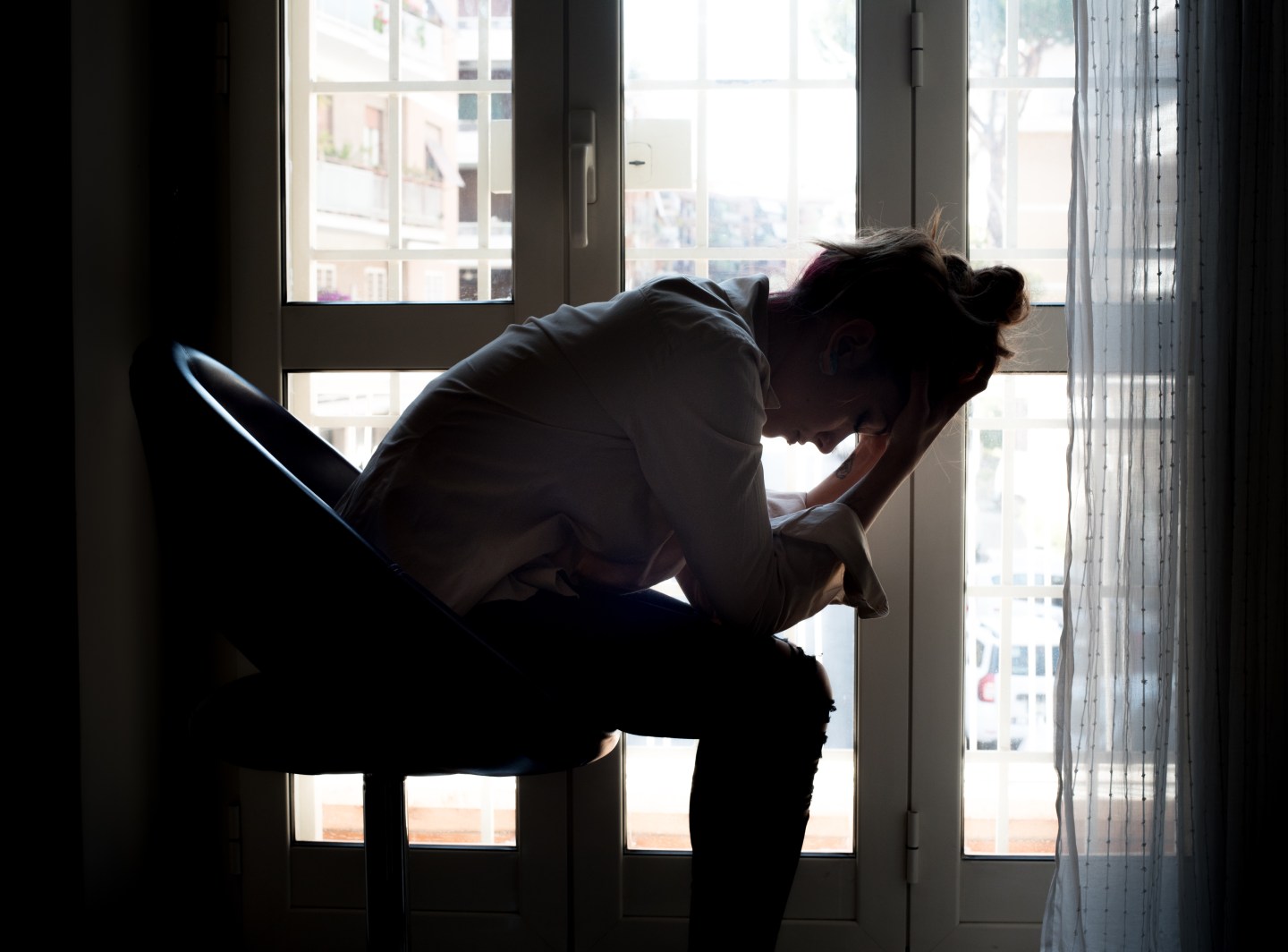 A depressed woman with her head in her hands in front of a window.