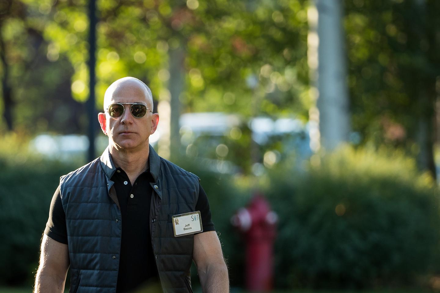 Jeff Bezos wears aviator sunglasses and a puffy vest. He looks as if he is walking with purpose.