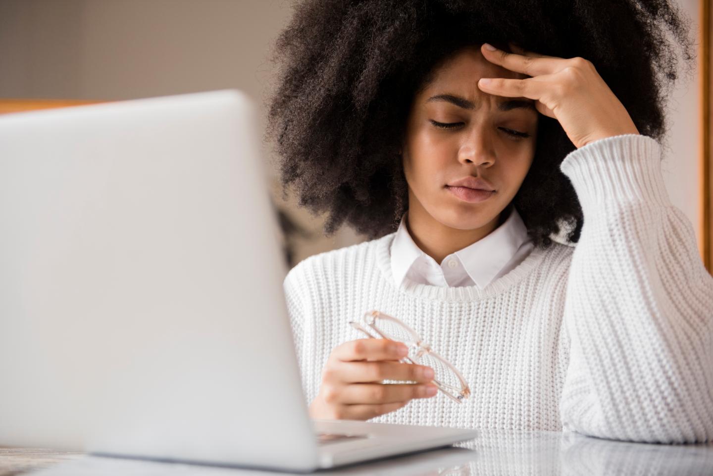 Frustrated woman holding eyeglasses at her laptop.
