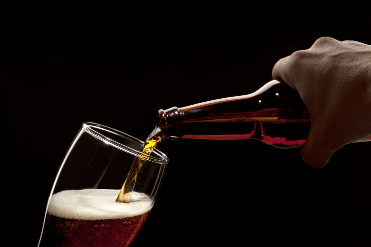 Hand Holding Beer Bottle Pouring Into Glass Isolated Over Black