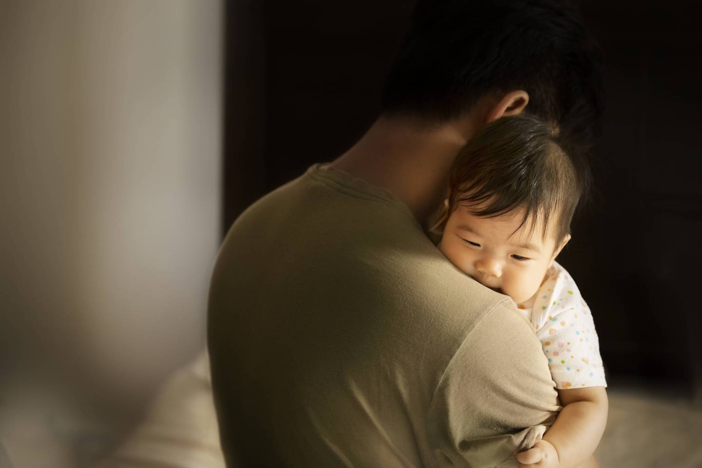 Toddler carried by father in moody bedroom background.