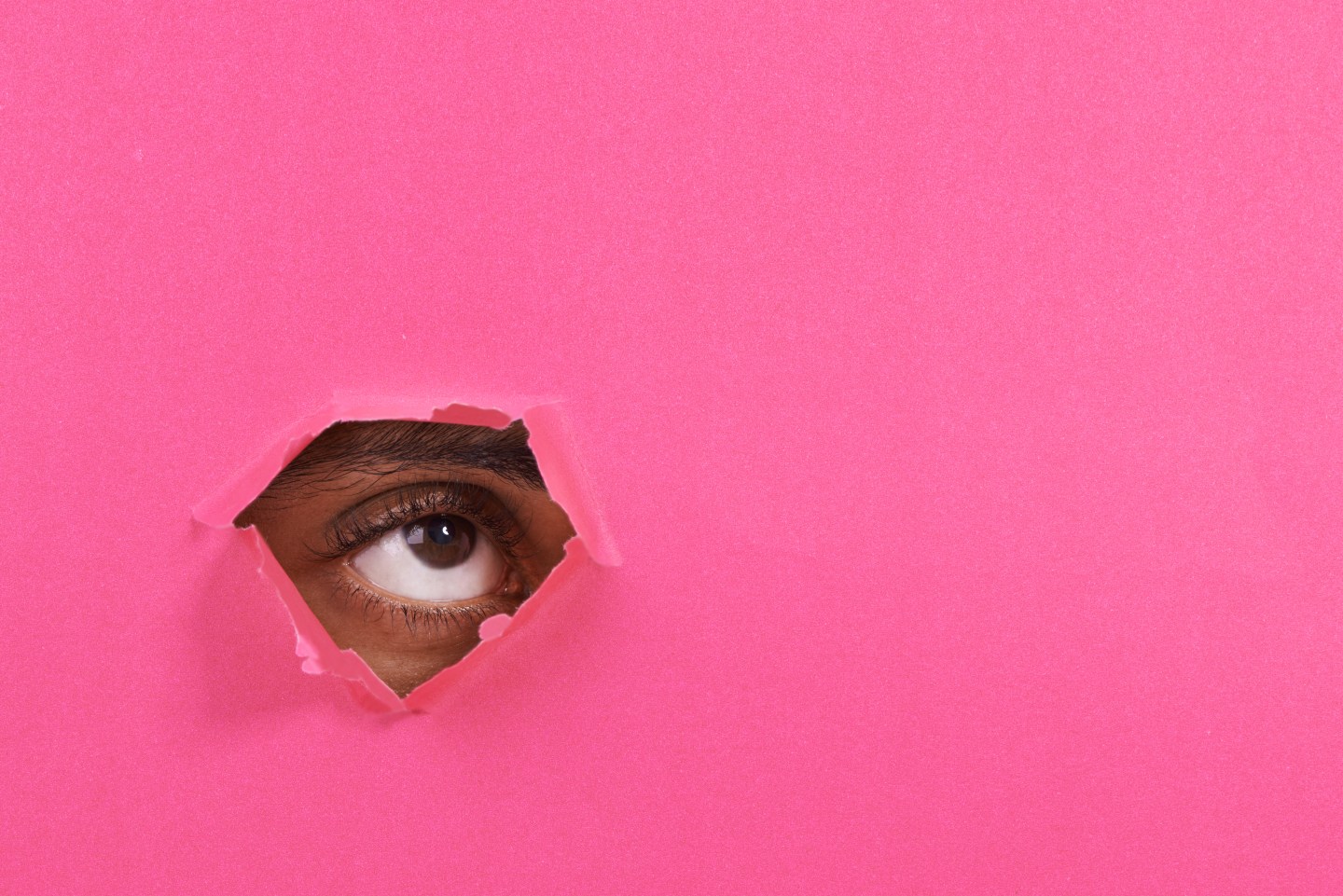 A view of a man's eye looking through a hole in some colorful paper