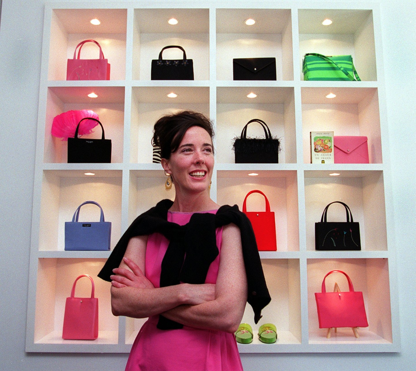 Designer Kate Spade poses in front of a wall of multi-colored handbags.