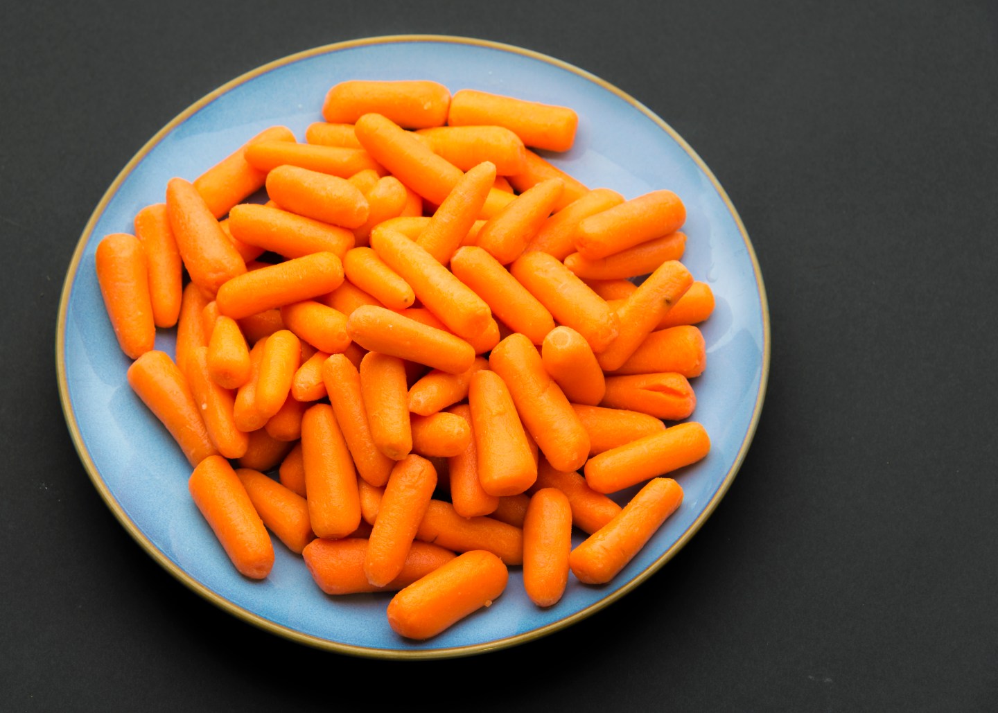 Baby carrots placed in blue plate against black background