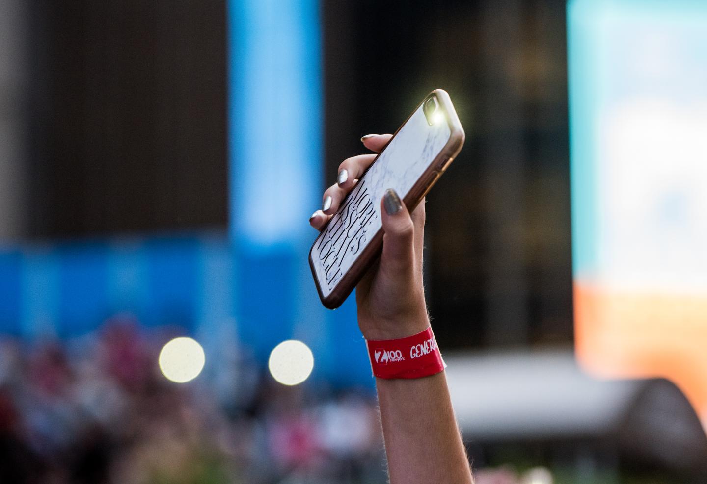 Someone holds aloft a cell phone at a music festival.