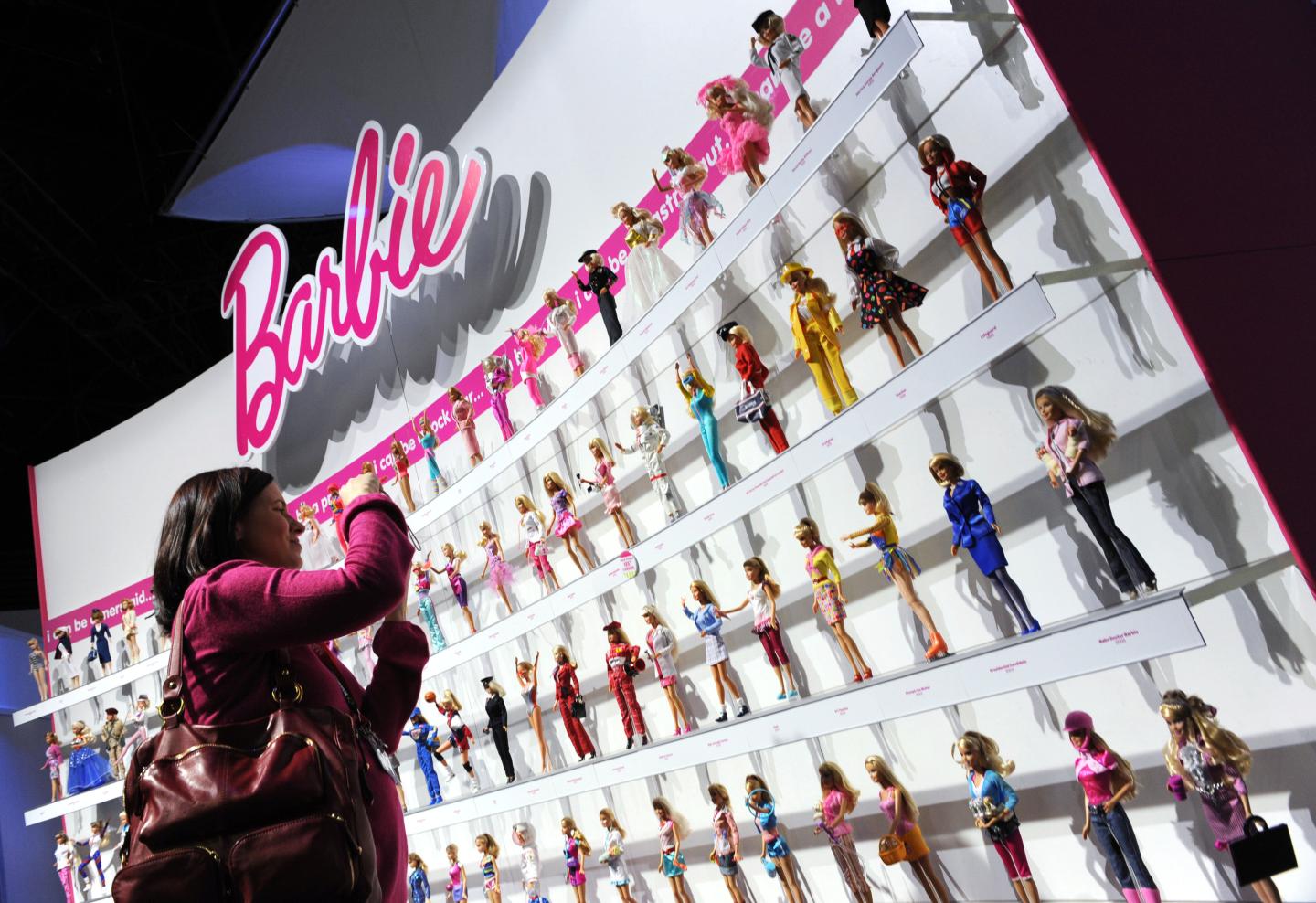 A woman photographs a wall of Barbie dol