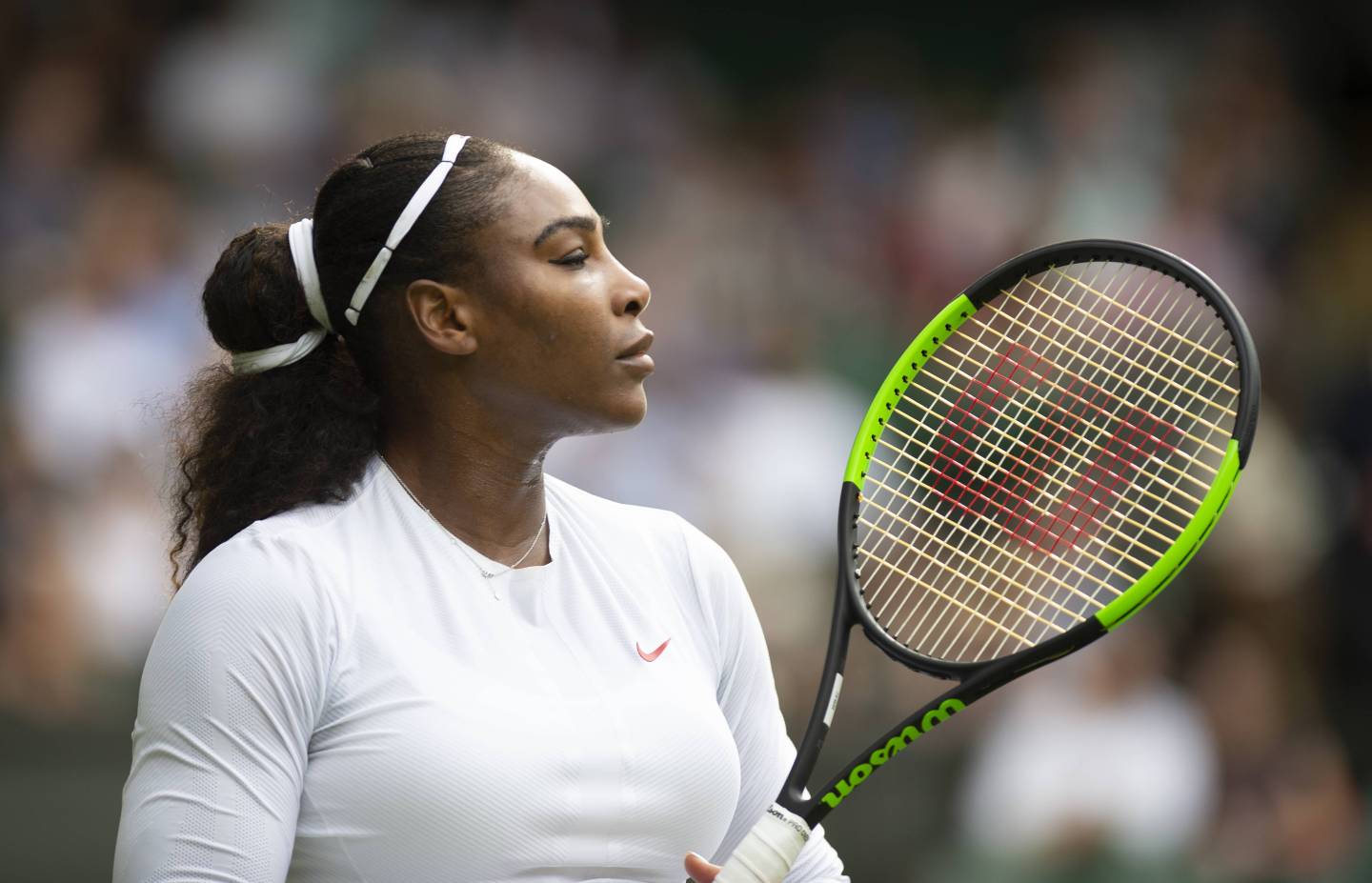 Serena Williams in profile at the Wimbledon courts holding a racket.