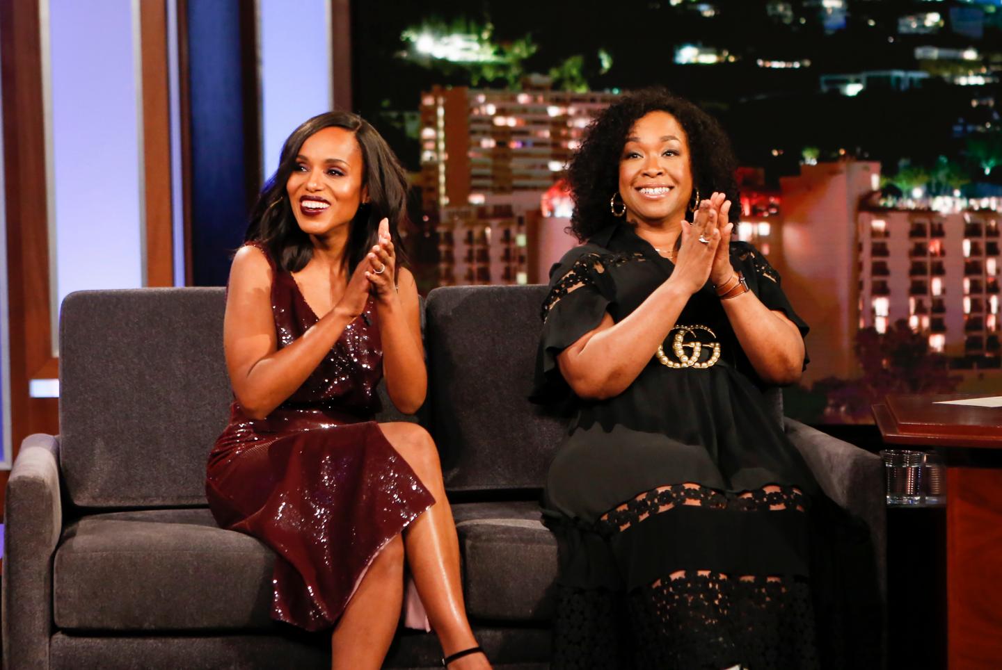 Kerry Washington and Shonda Rhimes sit side by side on a couch, clapping and smiling.