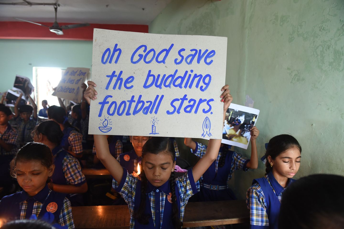 a boy holds a sign that reads "oh God save the budding football stars"
