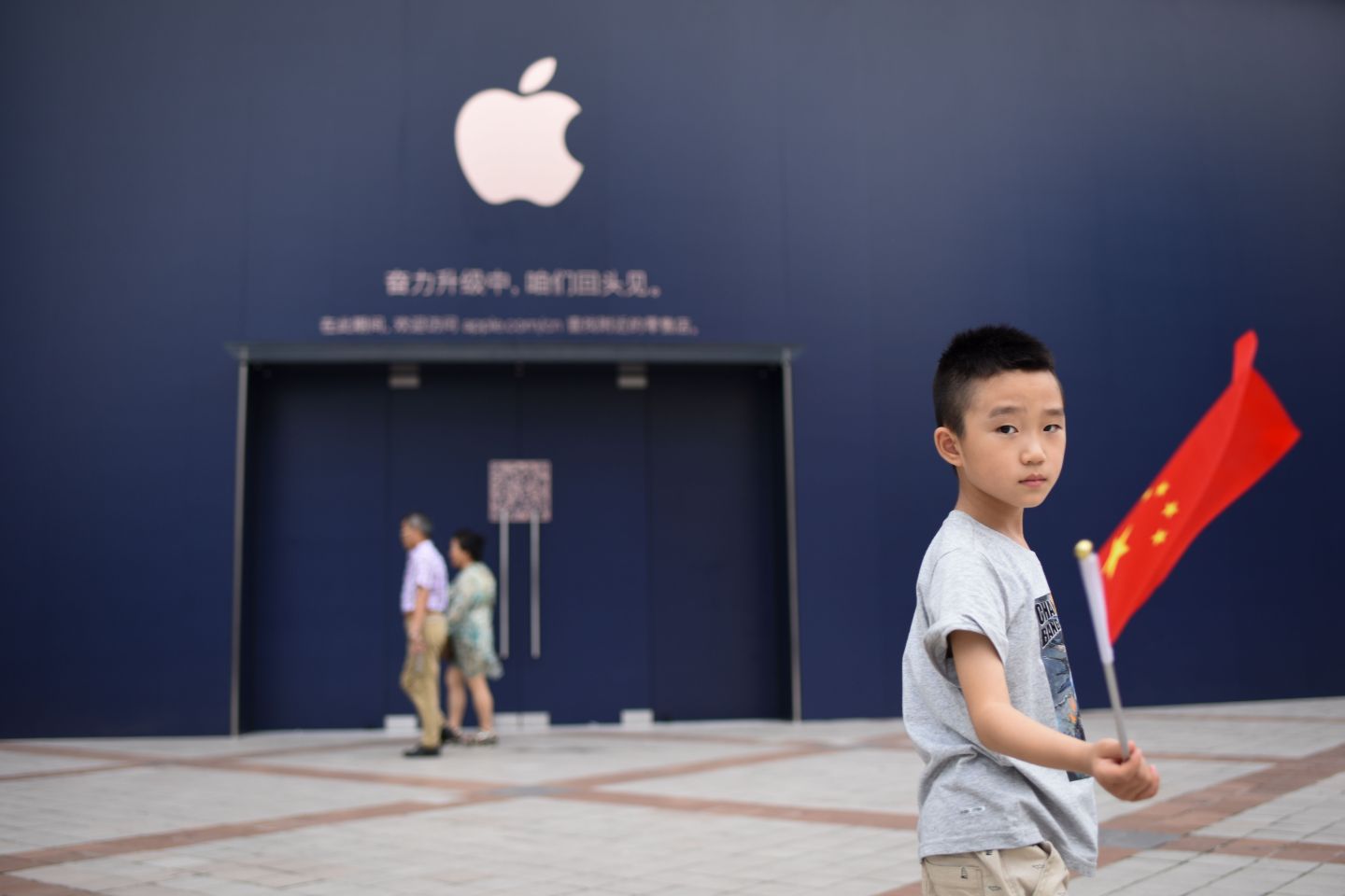 A boy holds a Chinese flag as he walks past an Apple Store undergoing renovation in Beijing on July 18, 2018.