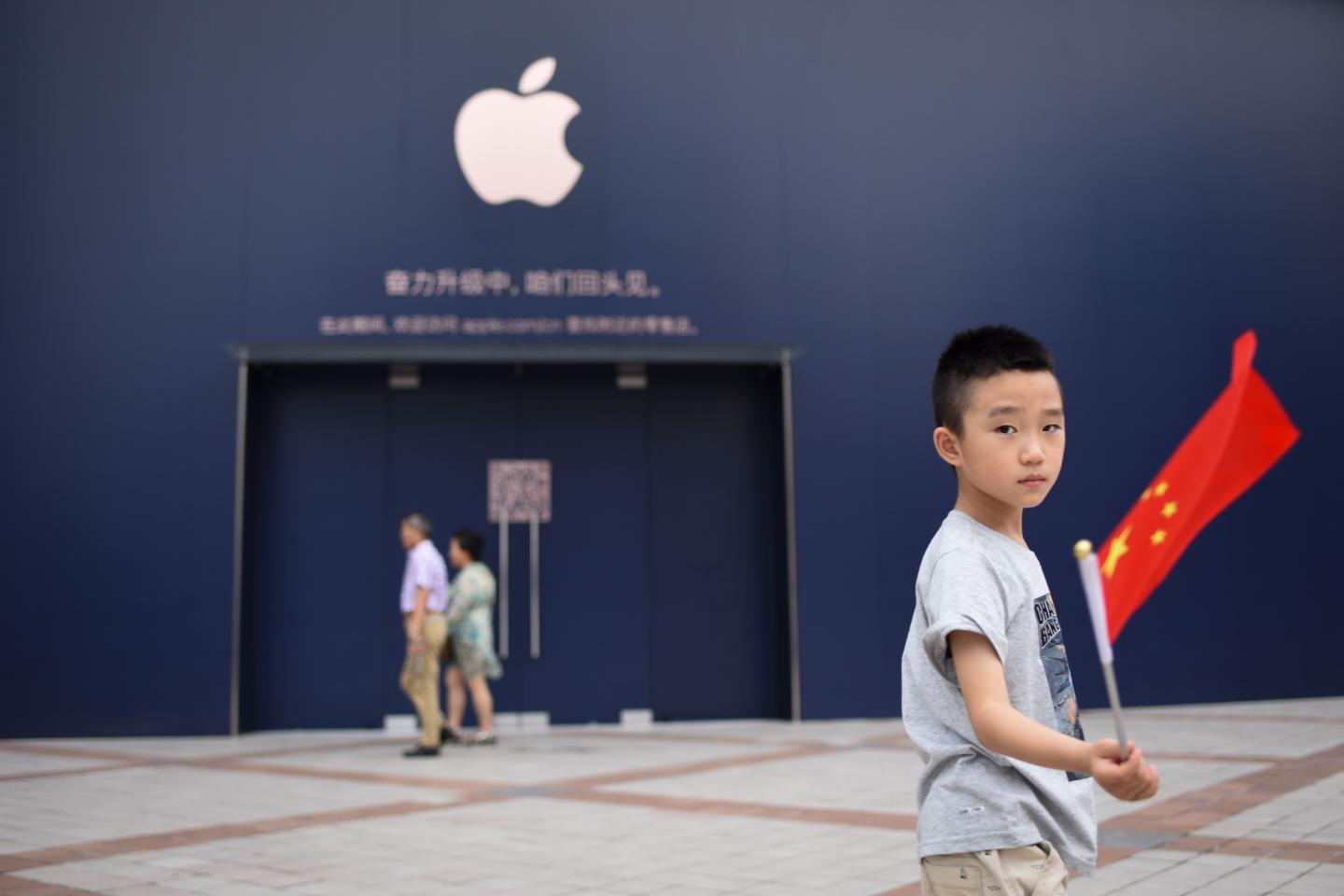 A boy holds a Chinese flag as he walks past an Apple Store undergoing renovation in Beijing on July 18, 2018.
