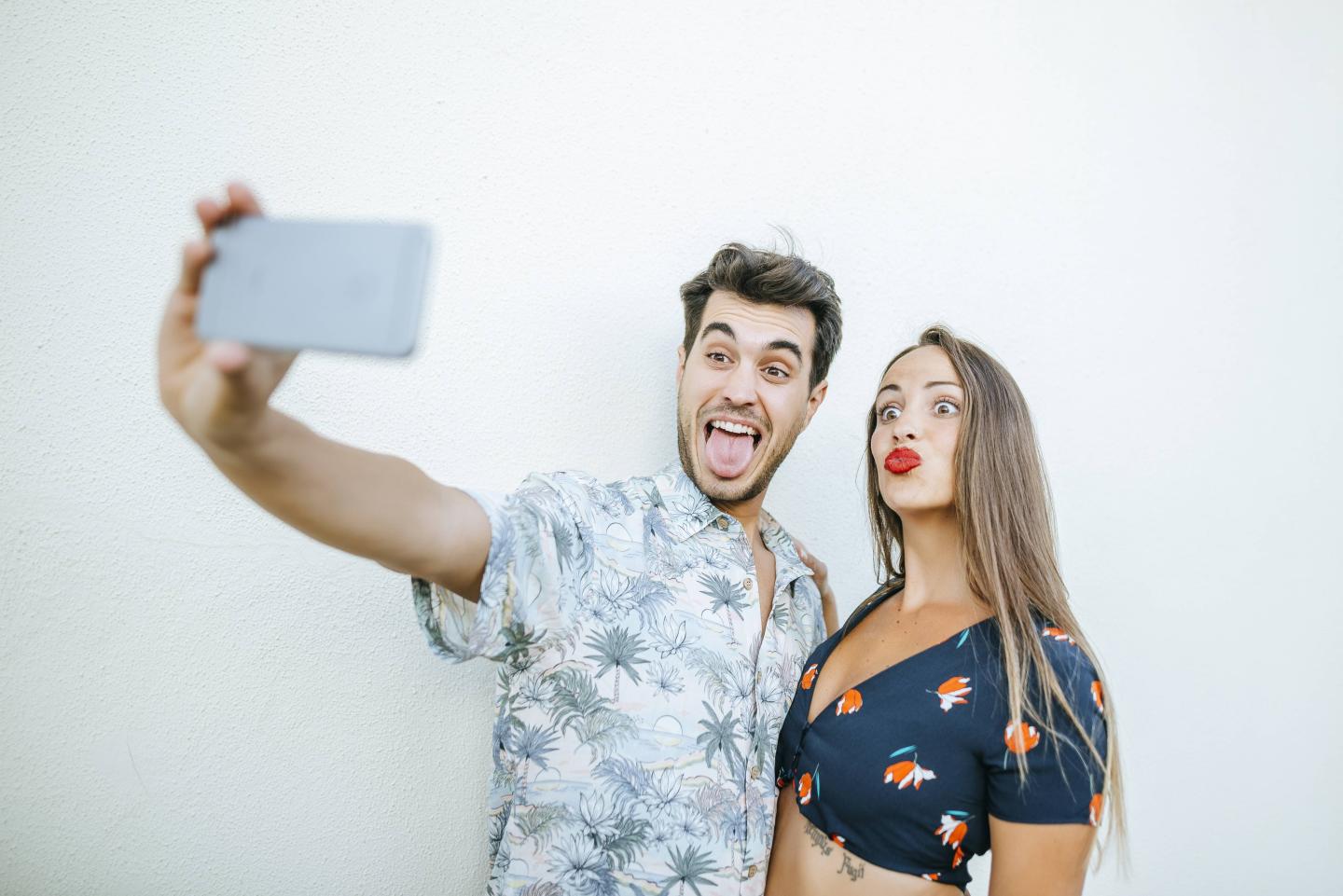 Playful couple taking a selfie with smartphone in front of white wall