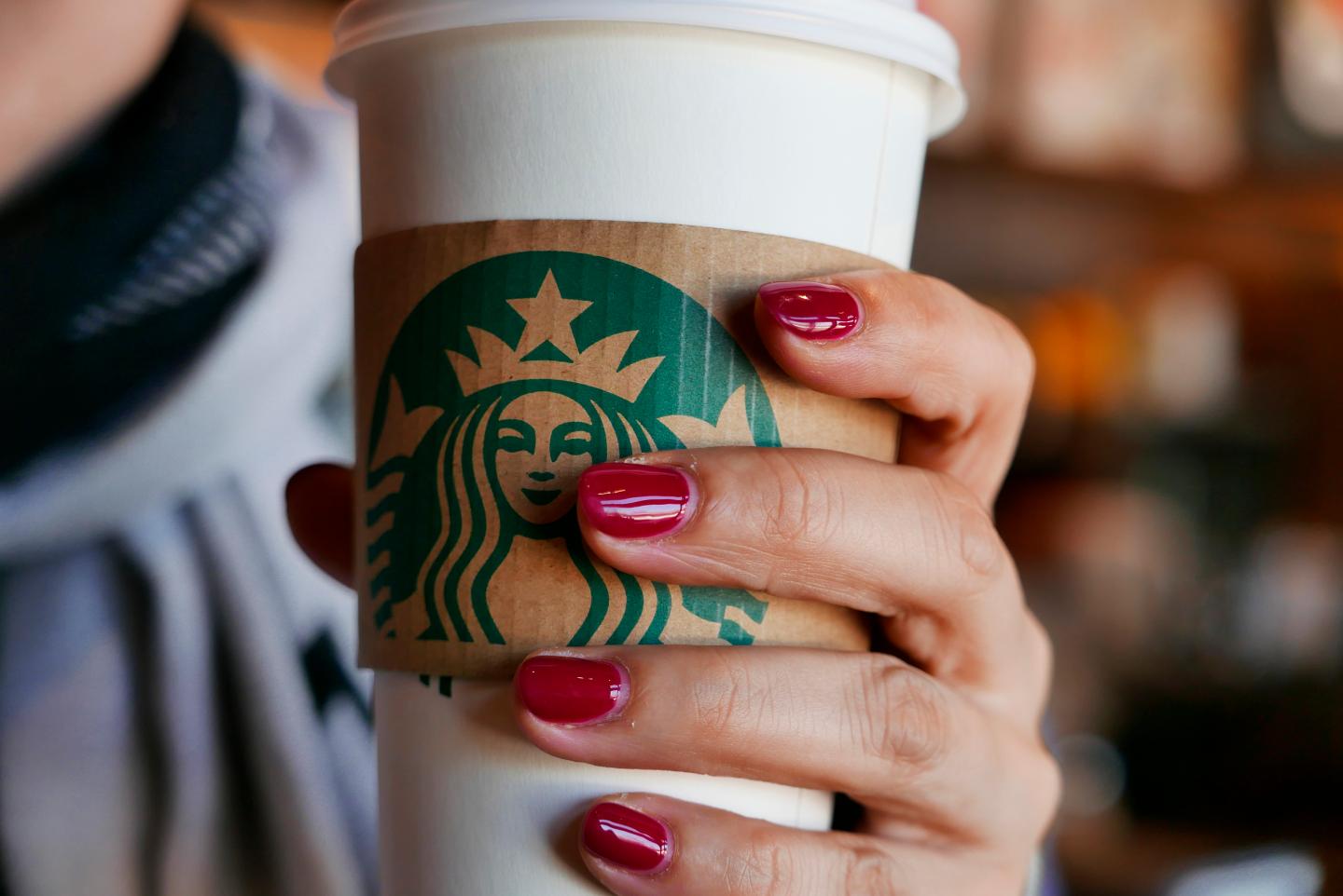 Hand holding a coffee cup in a Starbucks coffee shop. In