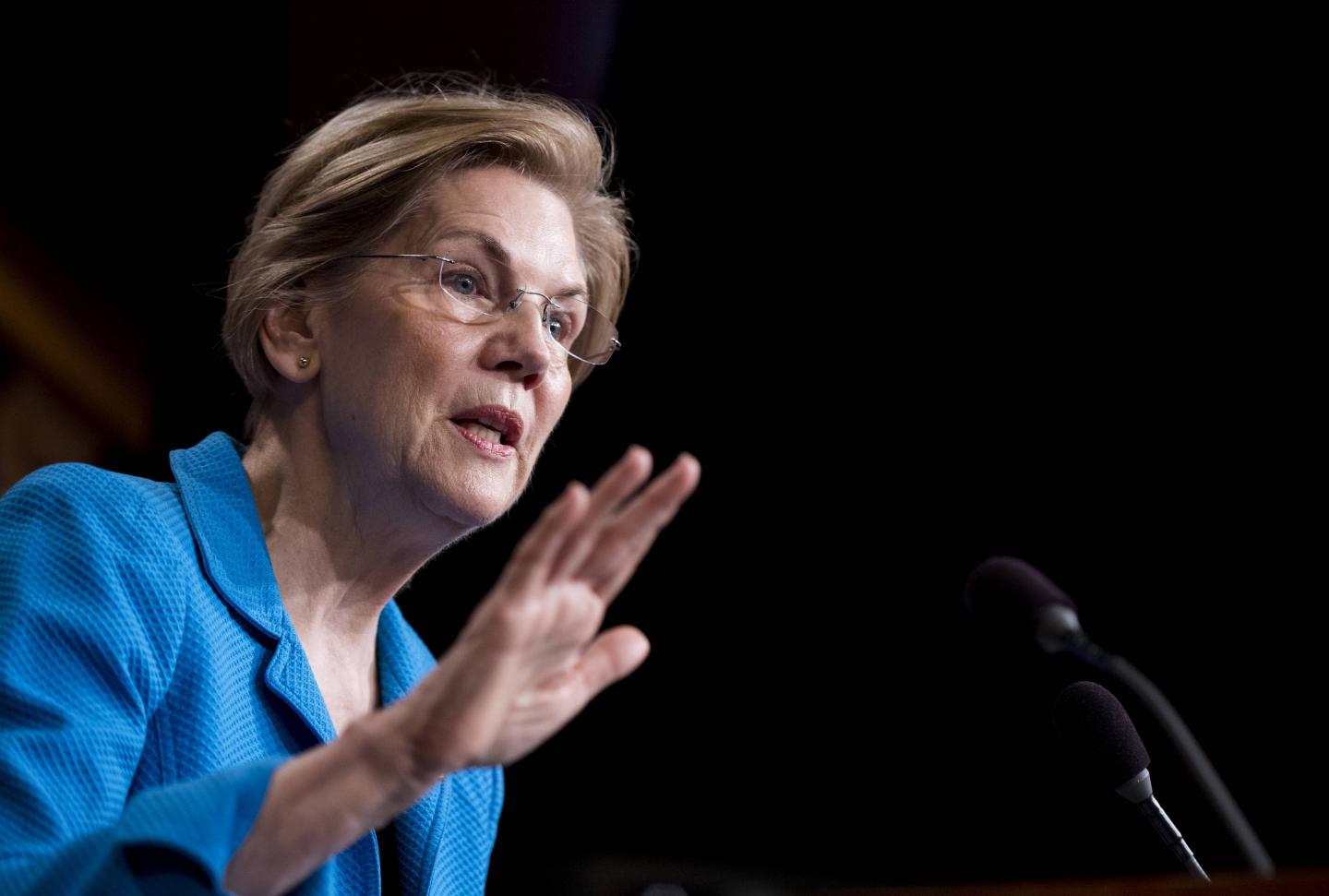 Sen. Elizabeth Warren speaks into a microphone, gesturing with her right hand