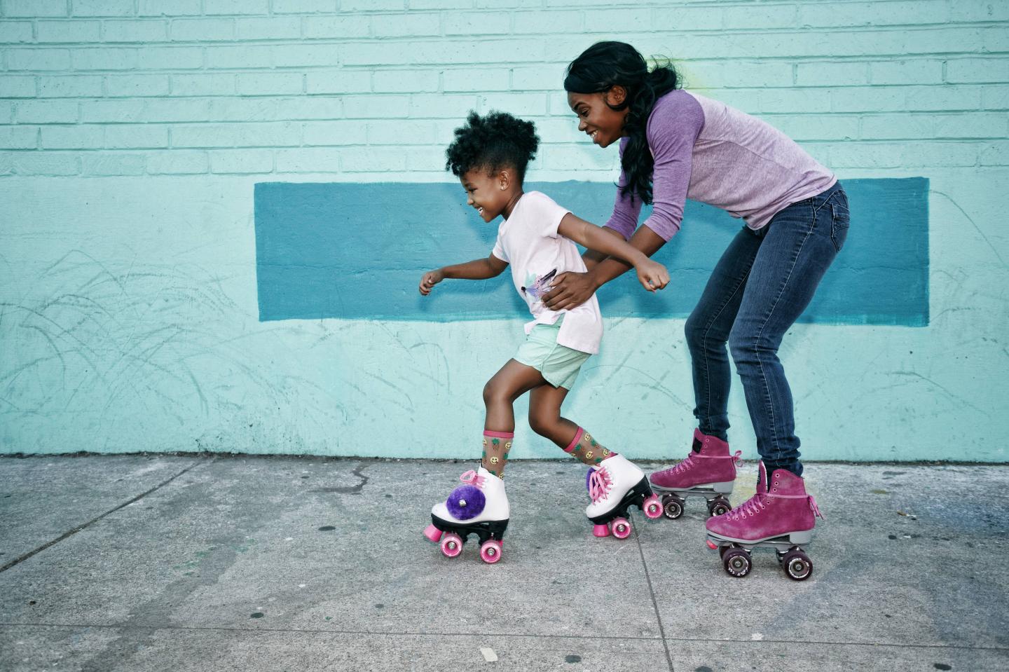 Mother holding waist of daughter wearing roller skates