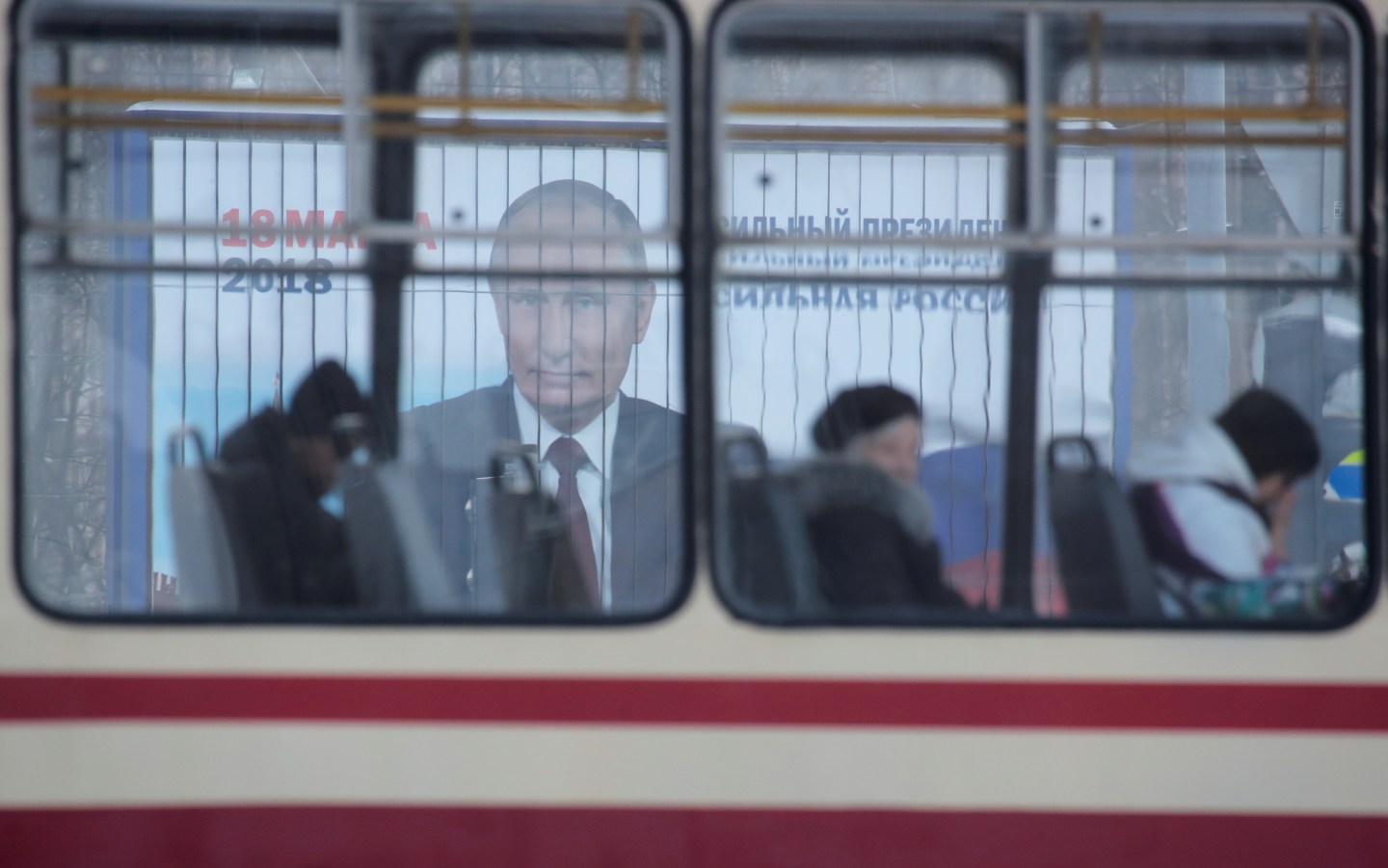 People ride a tram past a board, which advertises the campaign of Russian President Putin ahead of the upcoming presidential election, on a street in St. Petersburg