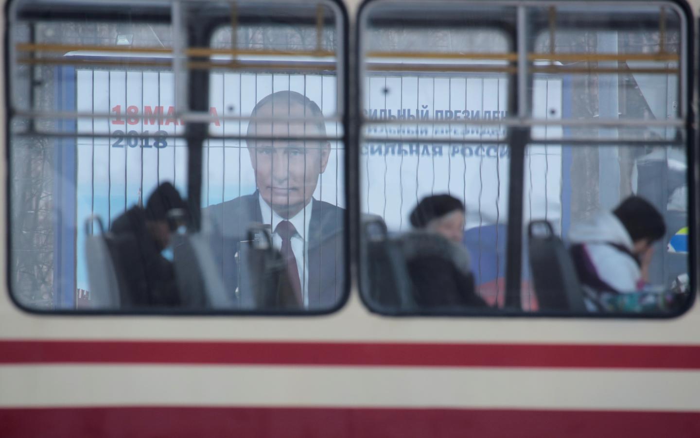 People ride a tram past a board, which advertises the campaign of Russian President Putin ahead of the upcoming presidential election, on a street in St. Petersburg