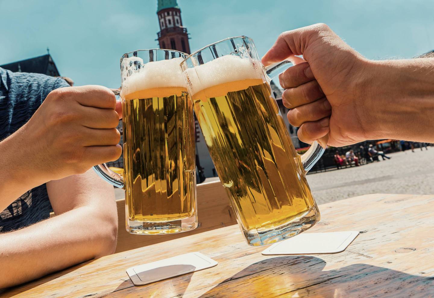 Cropped Hands Of Male Friends Toasting Beer Glasses At Table