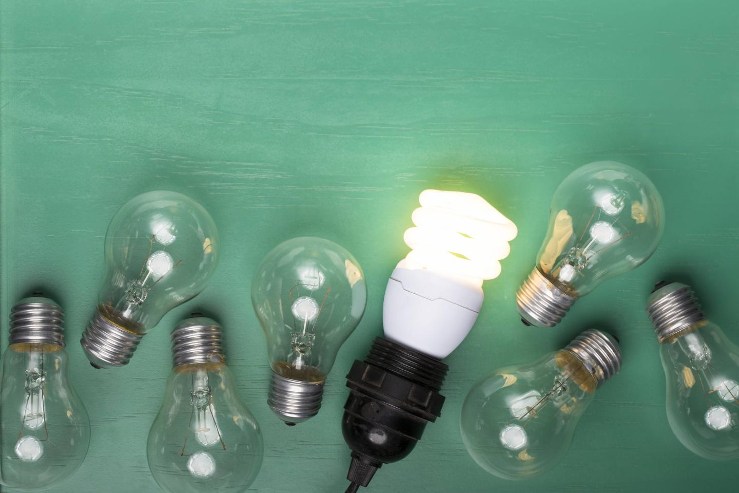 Incandescent lightbulbs laying next to one glowing, energy efficient lightbulb.