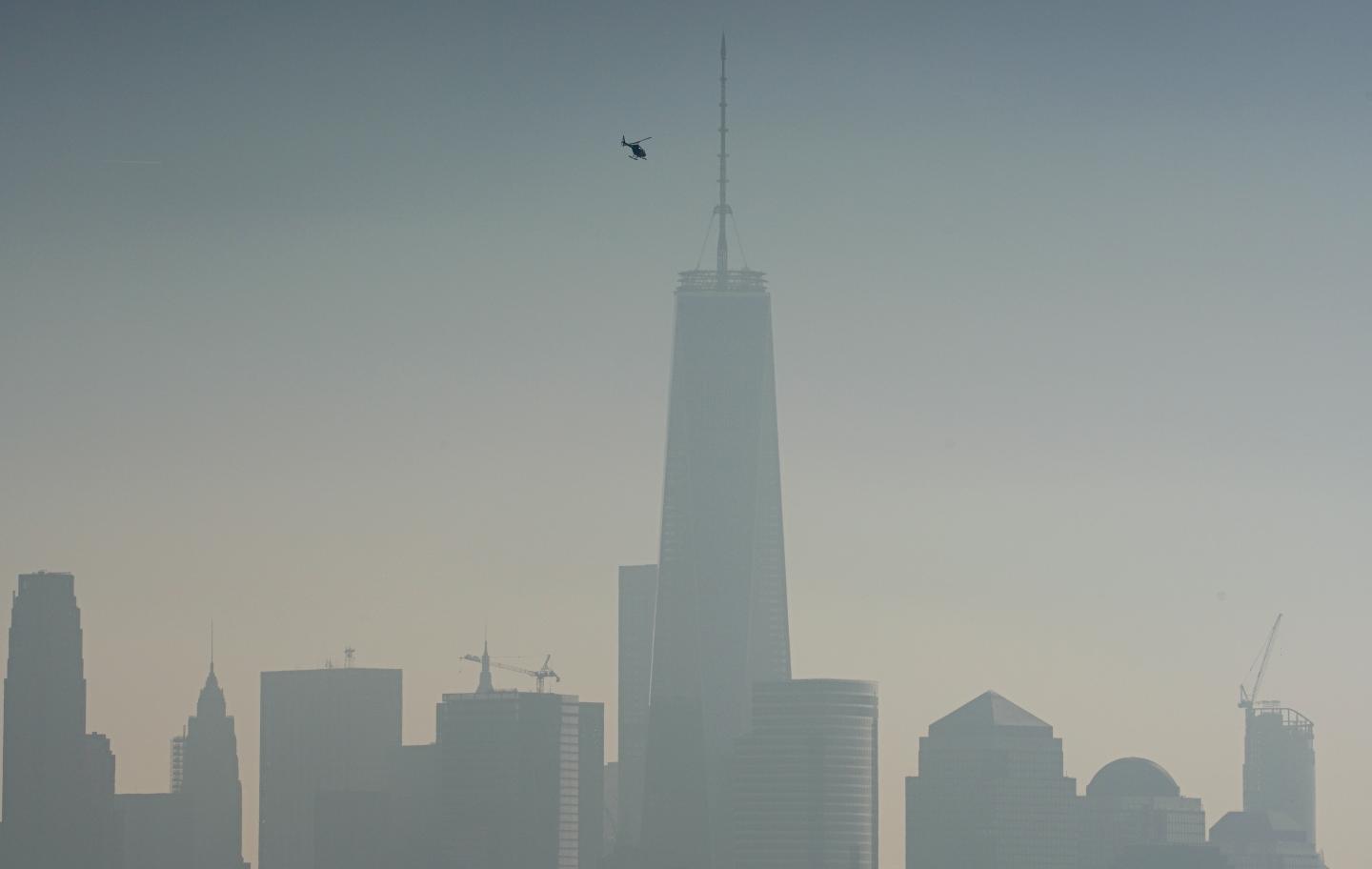 A helicopter flies over the Hudson River with One World Trade Center in the background in New York City