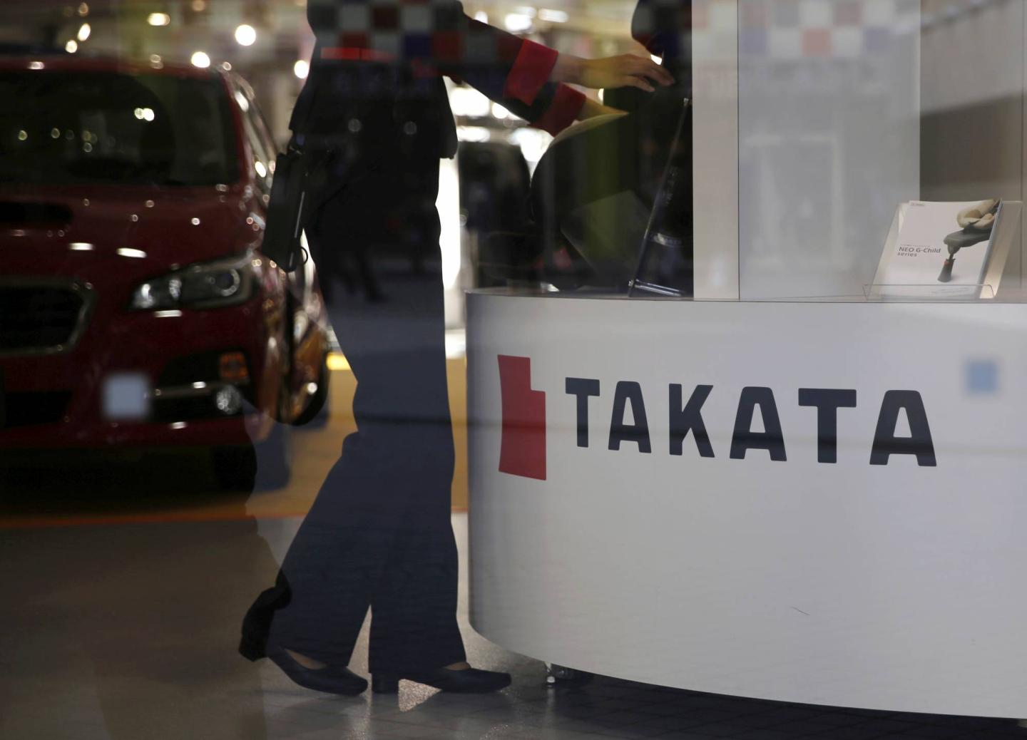 FILE PHOTO: A woman stands next to a logo of Takata Corp at a showroom for vehicles in Tokyo