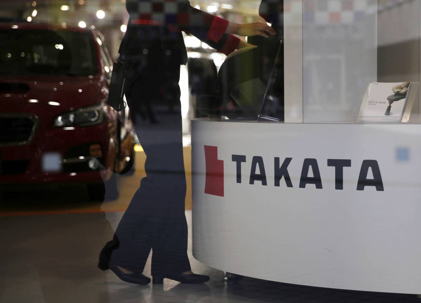 FILE PHOTO: A woman stands next to a logo of Takata Corp at a showroom for vehicles in Tokyo