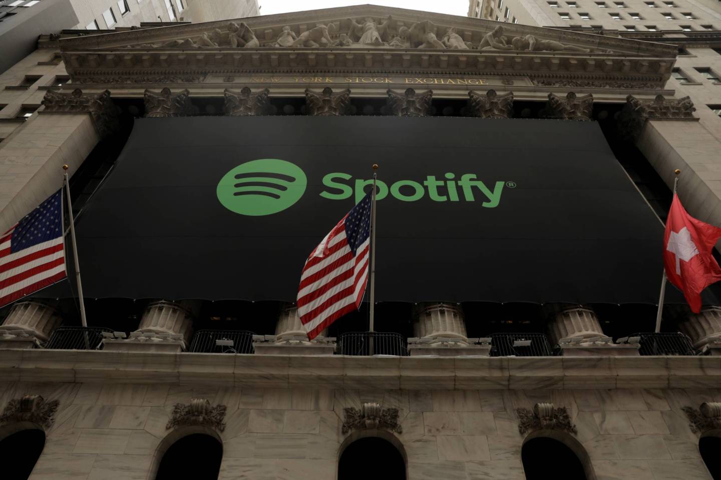 The Spotify logo hangs on the facade of the New York Stock Exchange with U.S. and a Swiss flag as the company lists it's stock with a direct listing in New York