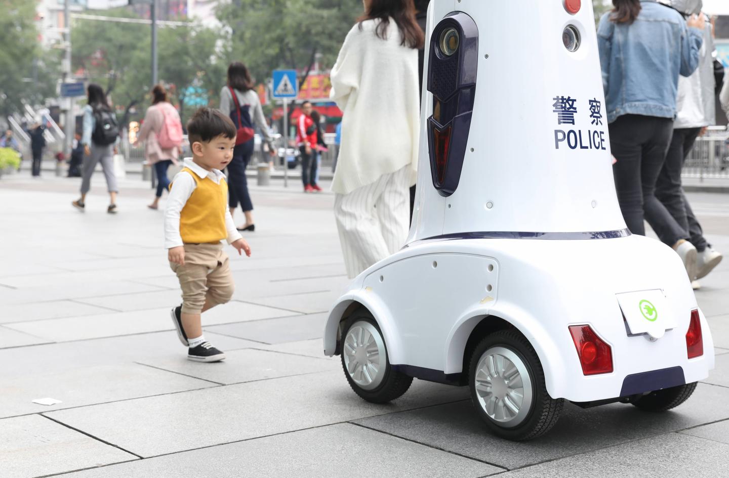 A child follows a police robot on duty in Xidan commercial district on Sept. 27, 2018, in Beijing, China.