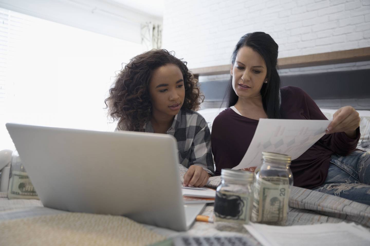 Mother with laptop teaching daughter personal finance management on bed