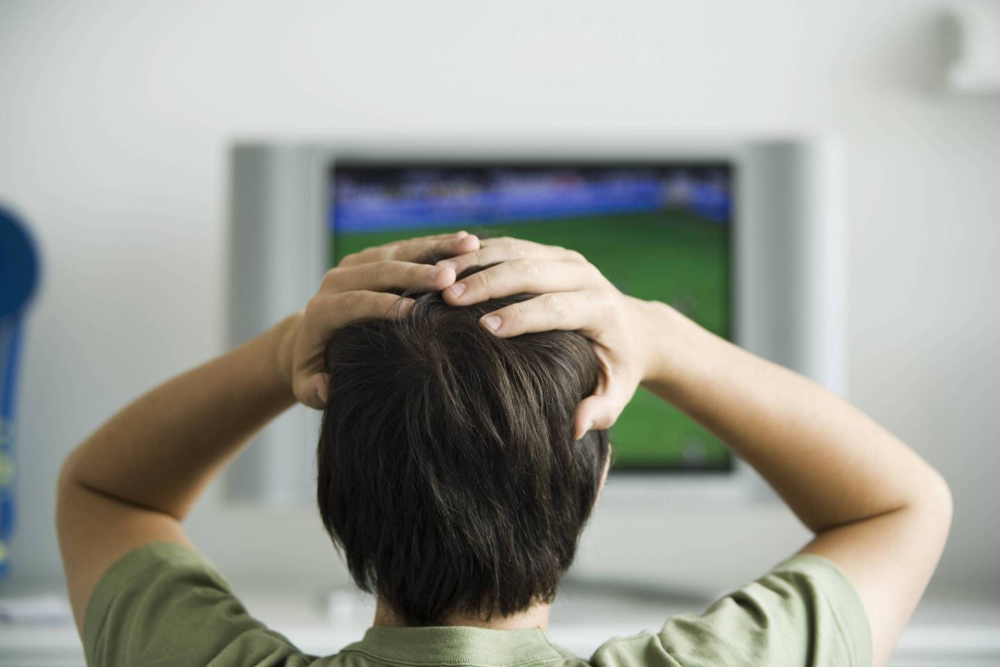 Male watching television, both hands on head, rear view