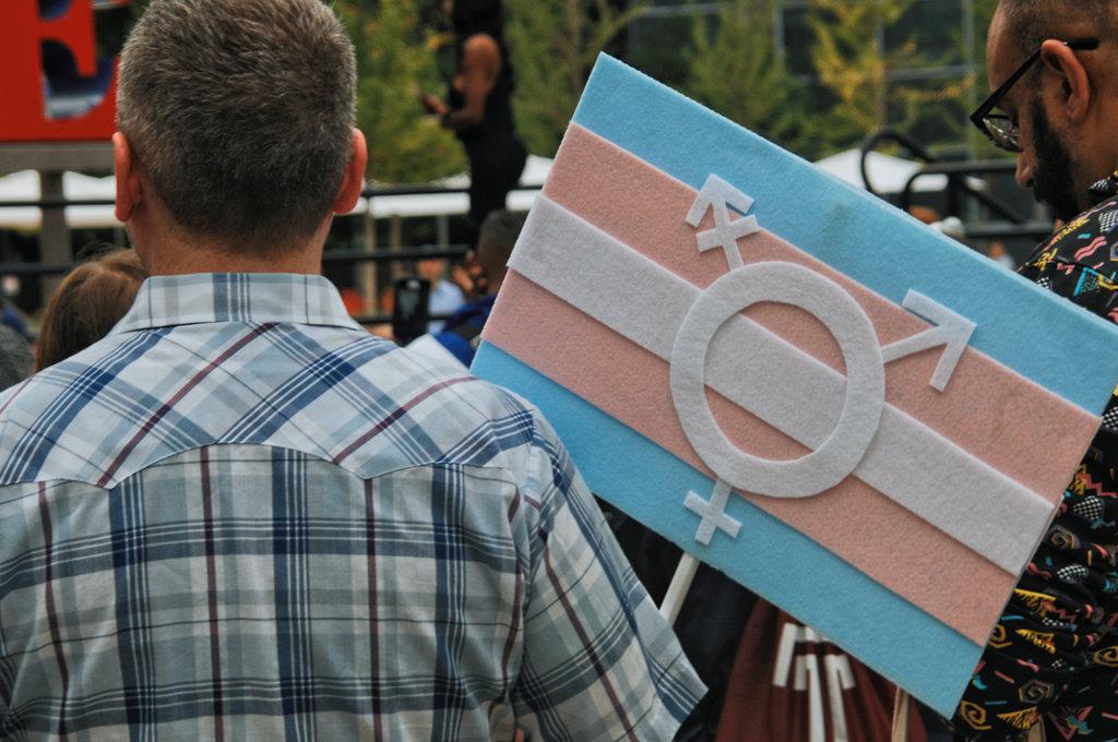 man stands with his back to the camera holding a trans flag