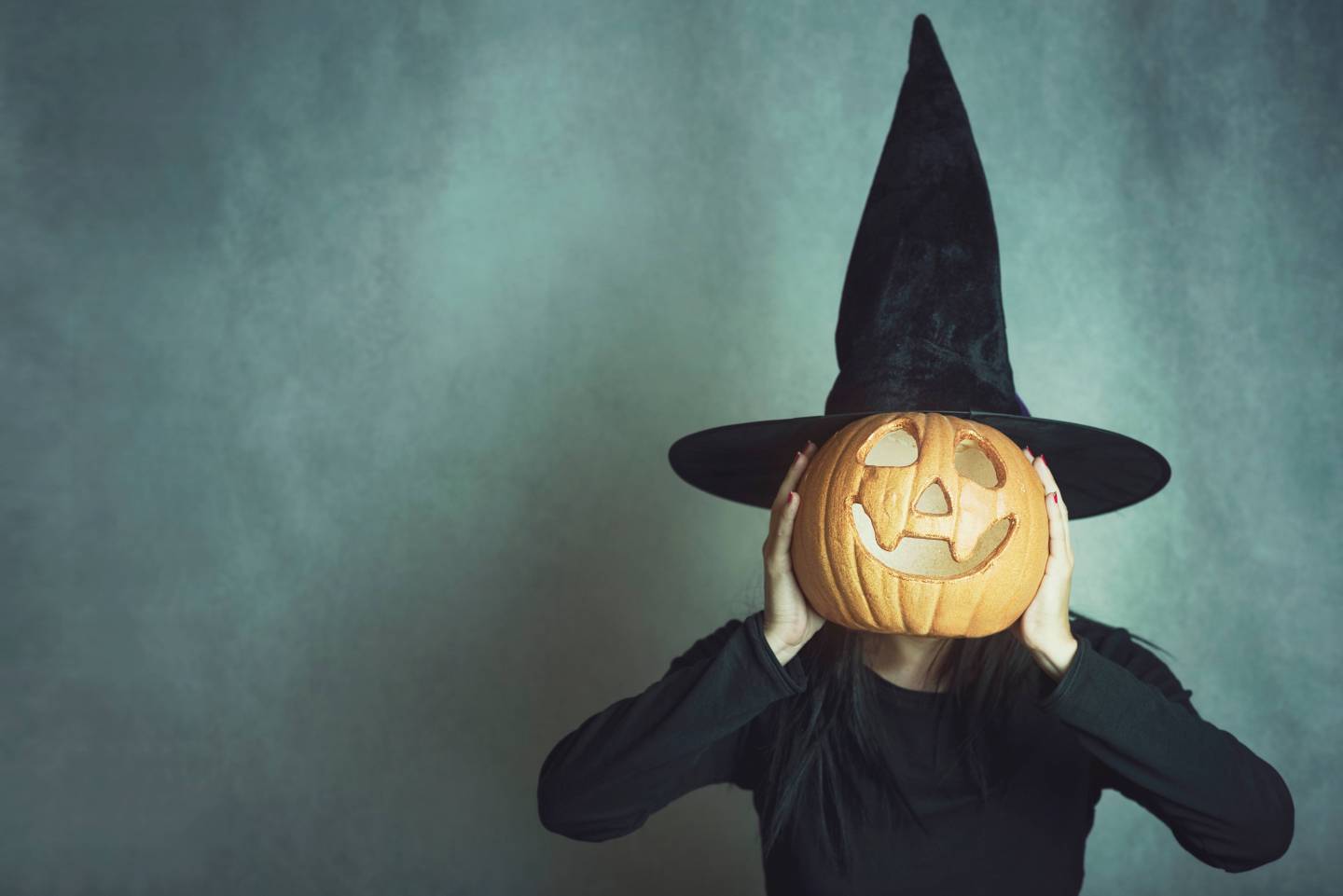 Woman Wearing Costume Covering Face With Jack O Lantern Against Wall During Halloween