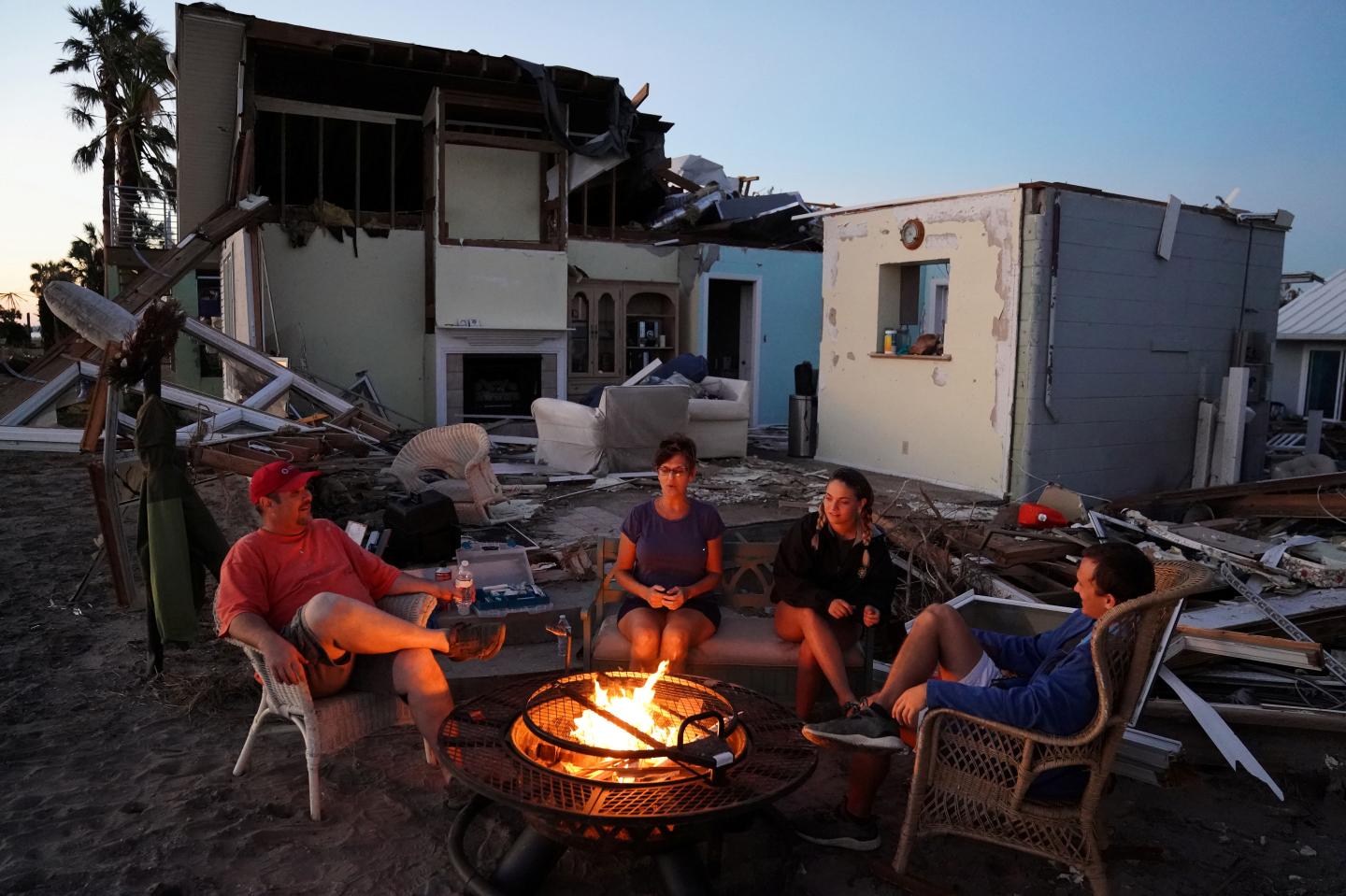 A family sits by a fire and prepares to eat a dinner of MREs in front of their house with no roof following Hurricane Michael in Mexico Beach, Florida