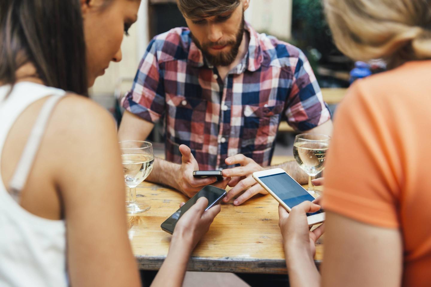Friends using cell phones and drinking spritzer at outdoor pub