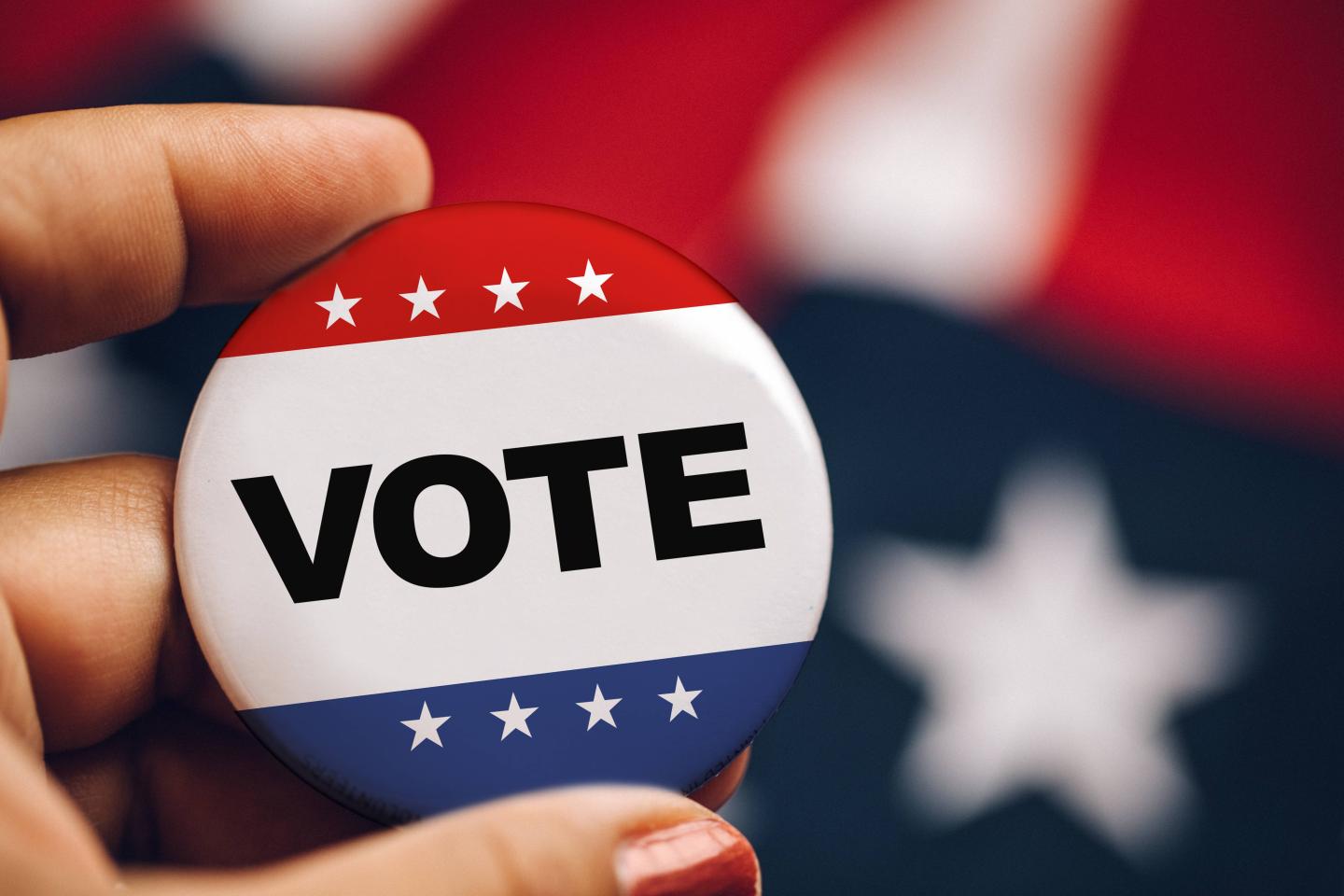 A woman's manicured hand holding a vote button.