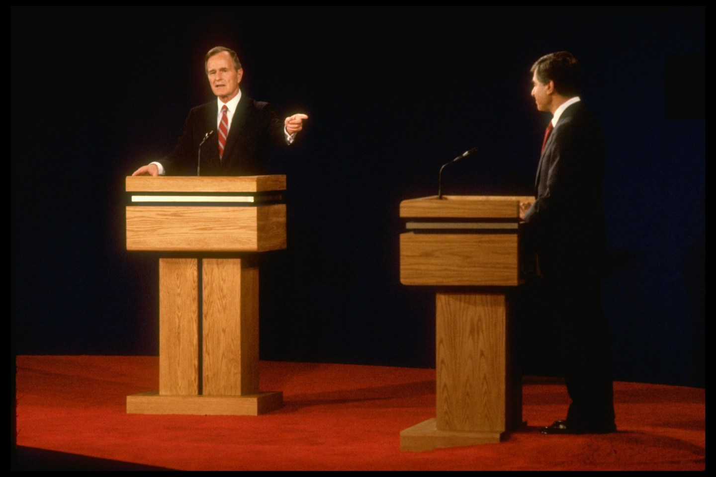 Democratic presidential candidate Michael Dukakis poised podium-side, facing his point-making Republican opponent VP George Bush (L) in first debate.