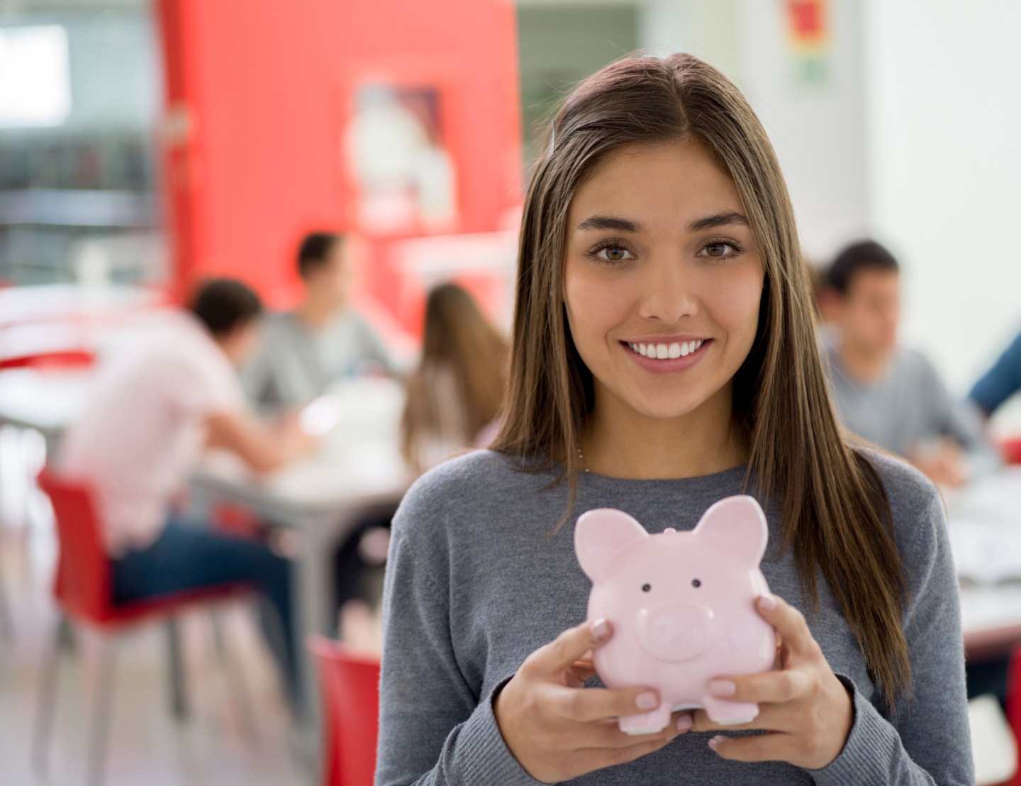Beautiful female student at the library holding a piggy bank looking at camera smiling