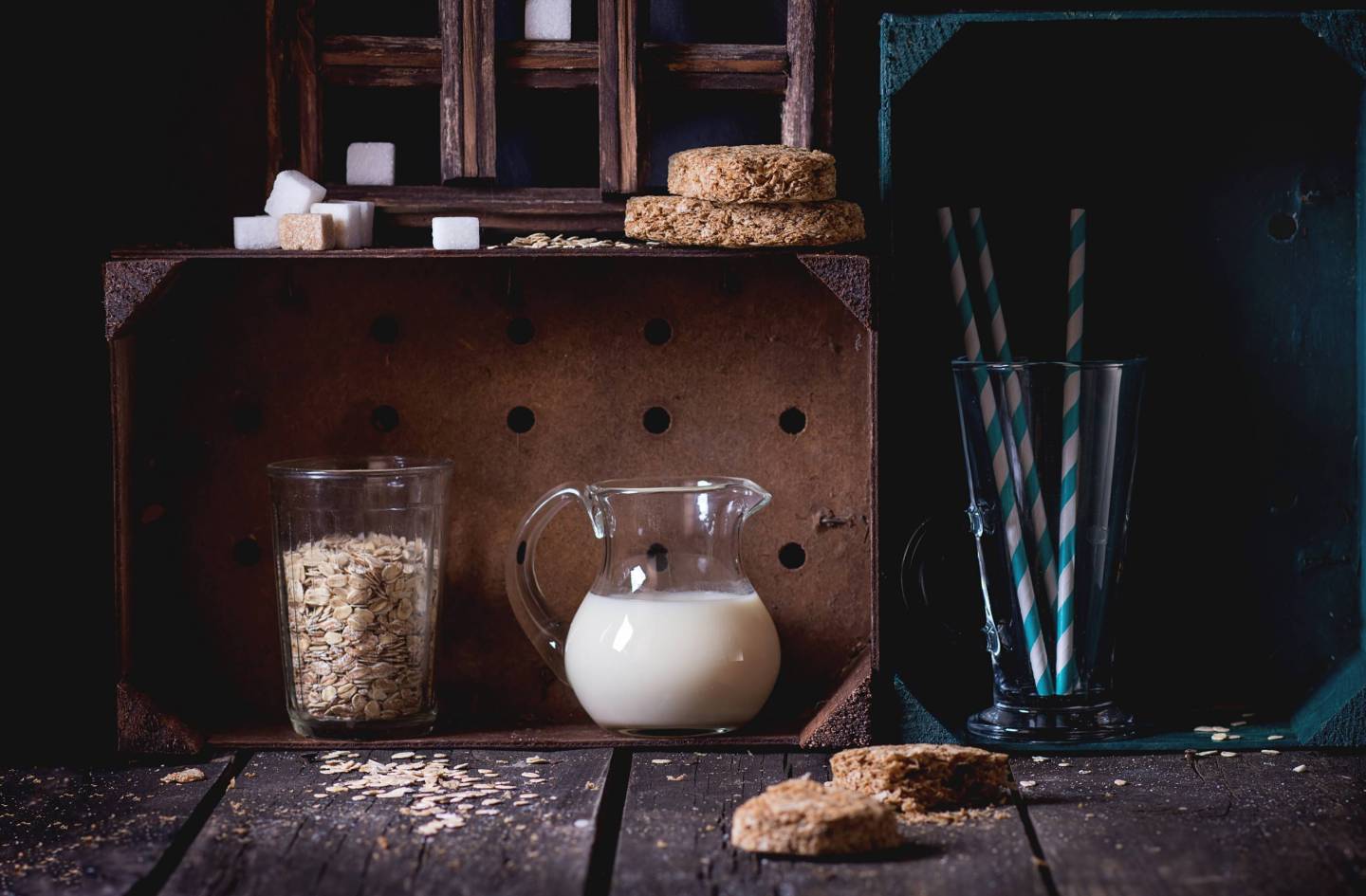 Glass jug of non-dairy oat milk and retro glass of oat flakes with sugar cubes and crispbread in wooden kitchen cabinet over old wooden table. Dark rustic style.