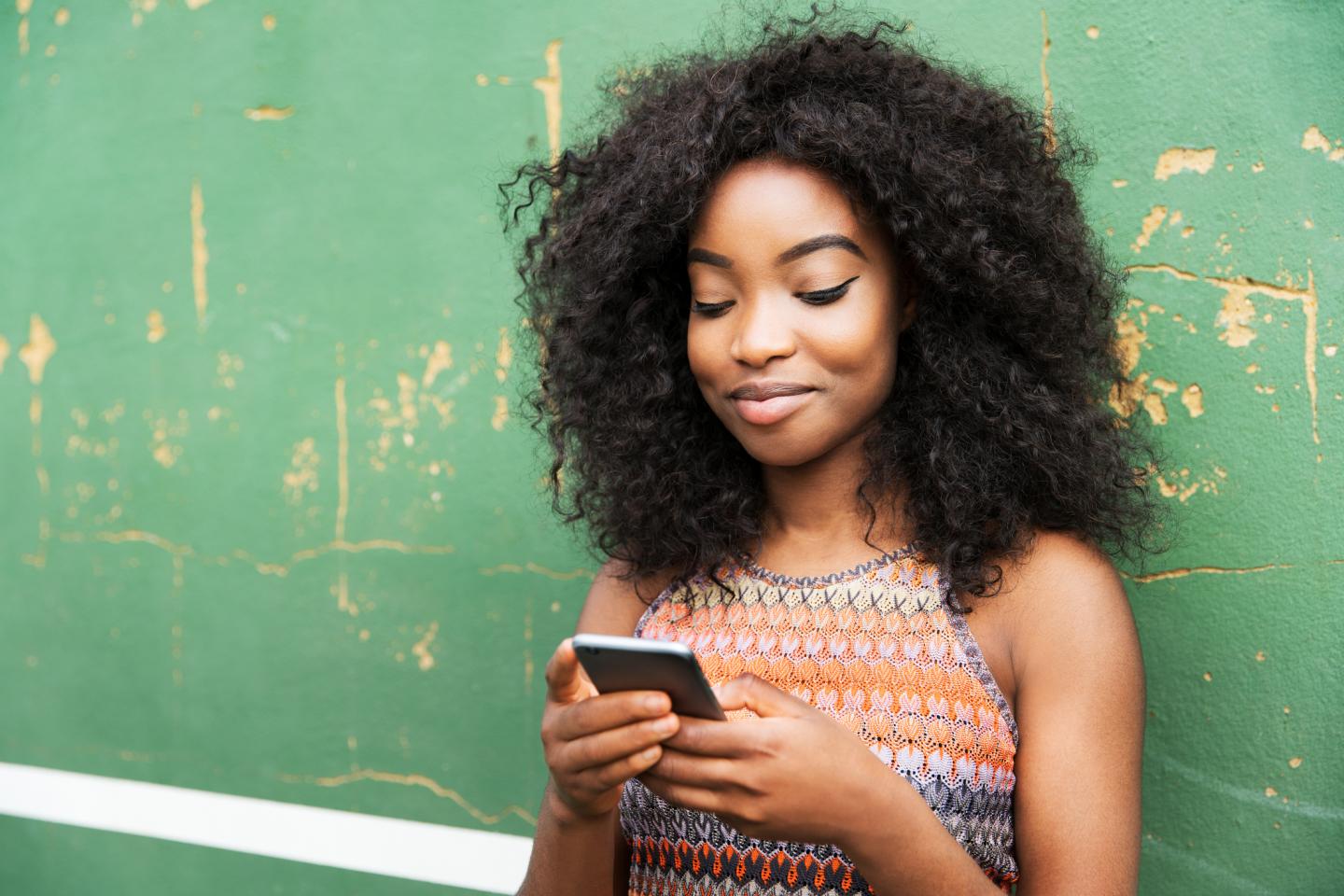 Woman using smart phone next to green wall