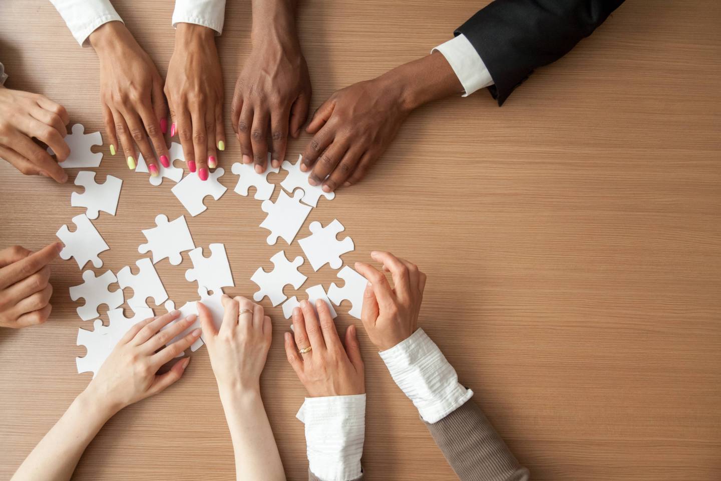 Hands of multi-ethnic team assembling jigsaw puzzle, viewed from above the table