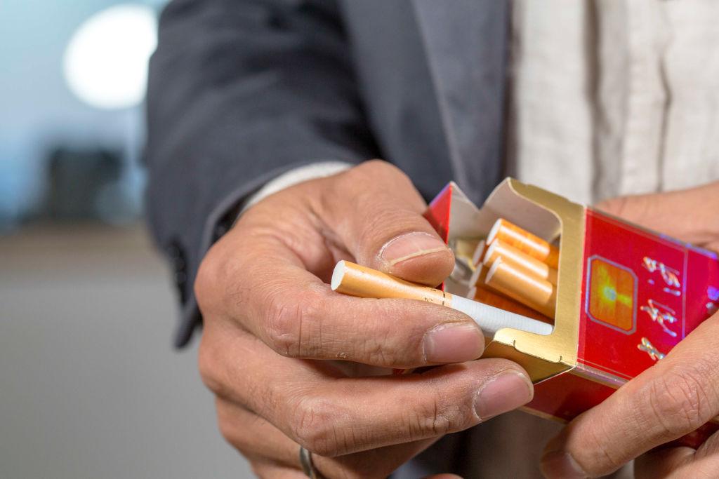 A man is drawing out a cigarette from a cigarette box.